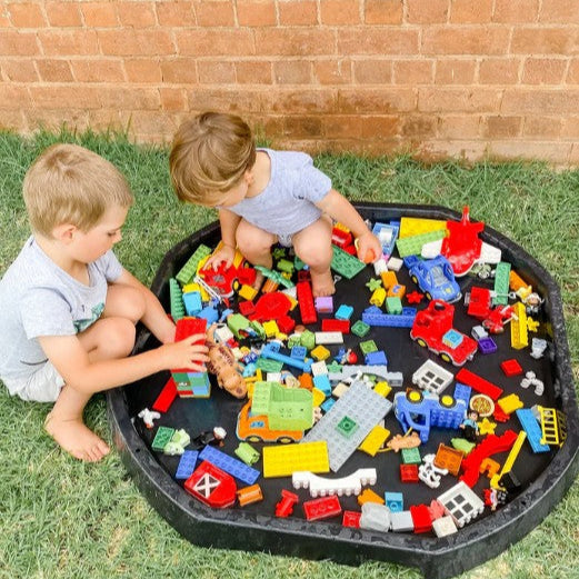 Two children playing with colorful building blocks on a black tray outdoors.